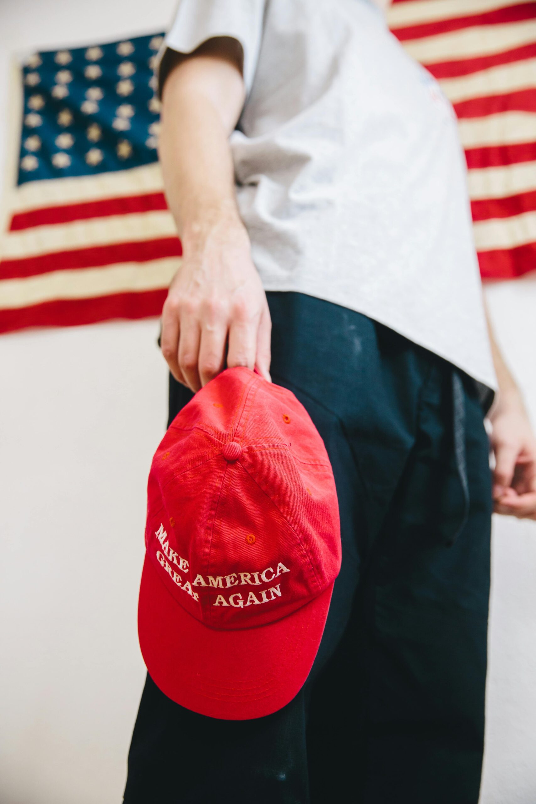 A person holding a 'Make America Great Again' hat against a backdrop of the American flag.