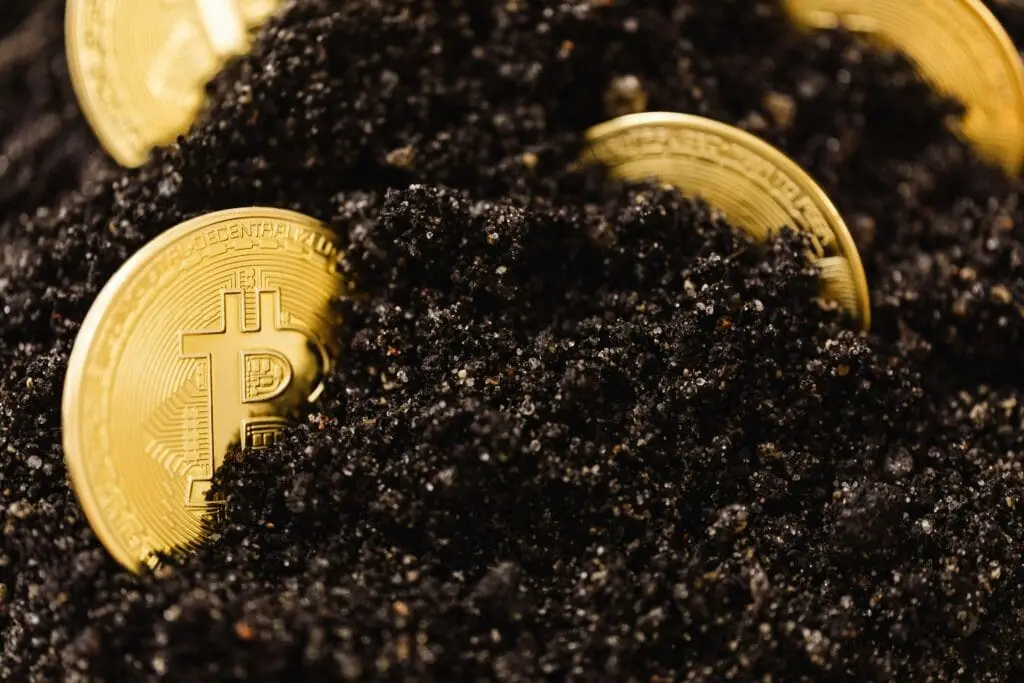 Close-up of Bitcoin coins partially buried in dark, textured soil, representing digital currency growth.
